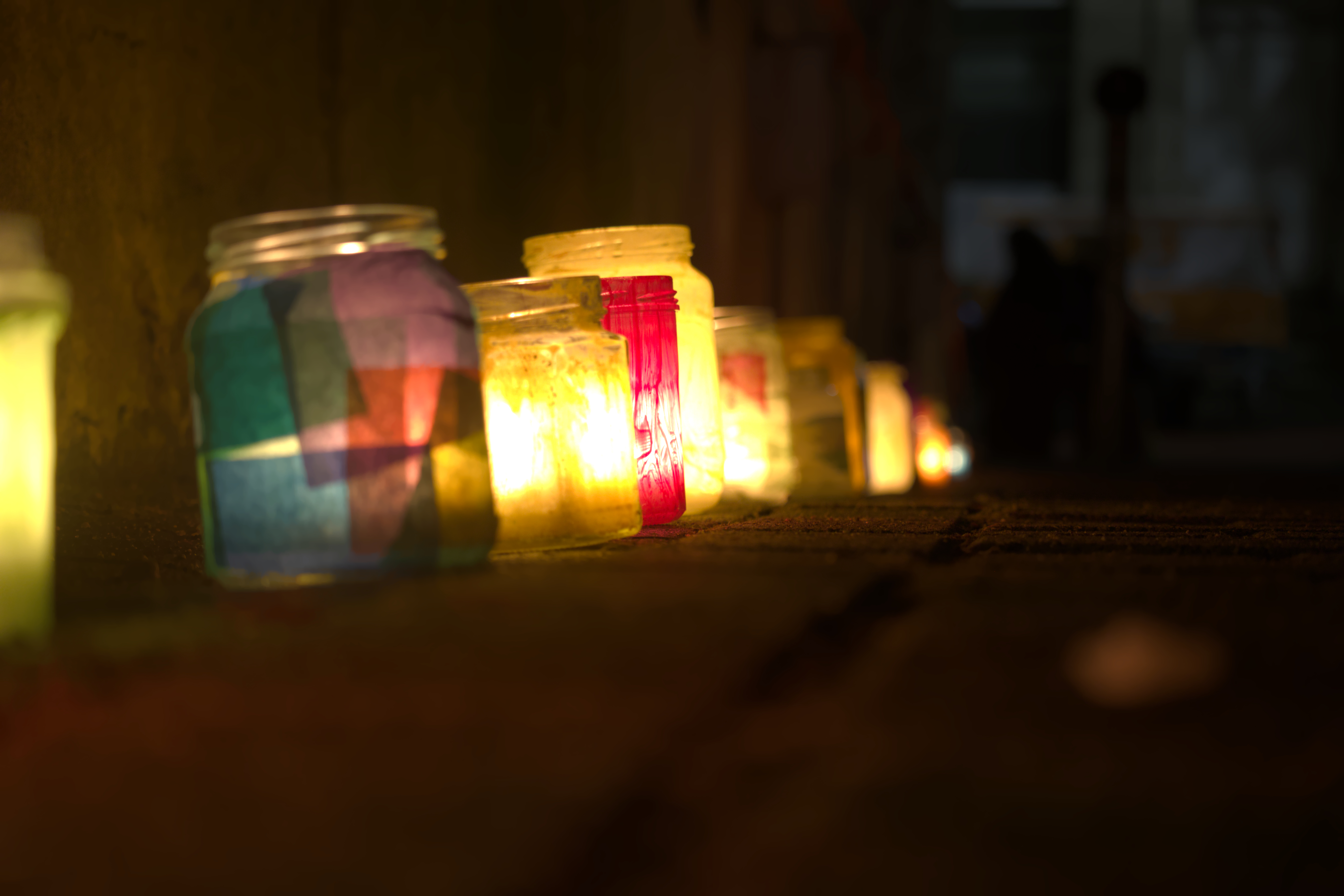 A row of colorfull glasses filled with candles glowing onto the pavement